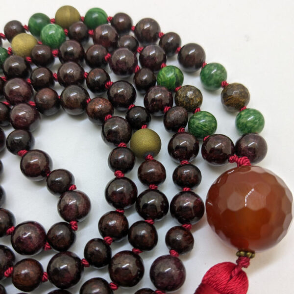 punased, rohelised ja pruunid ümmargused kristallid pärlid. oranz Karneooli Guru ehk õpetaja kivi. 108 pärliga Mala palvehelmed kaelakee. Punane siidi tutt. Heledal taustal