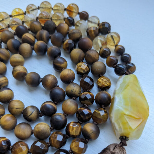 Pruunid ja kollased ümmargused kristallid pärlid. Kollane Ahhaat kristall Guru ehk õpetaja kivi. 108 pärliga spirituaalne Mala palvehelmed kaelakee. Pruun tutt. Heledal taustal