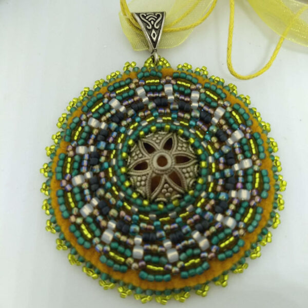 rohelised ja kollased helmed tikitud Mandala kaelakee. Keskel on metalne prossist südamik. Mandala on loodud helmestikandina. Kollane pael. heledal taustal.