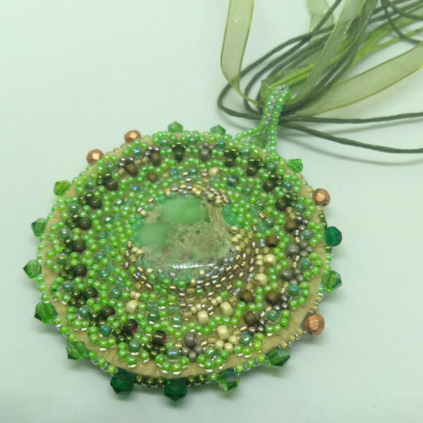 Rohelised helmed tikitud Mandala kaelakee. Keskel on VARISTSIIT kristallist südamik. Mandala on loodud helmestikandina. Roheline pael. heledal taustal.