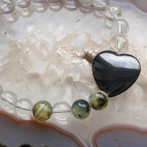 valged, rohelised ümmargused kristalli pärlid käevõrus. Must kristallist süda. taustal erinevad kristallid.