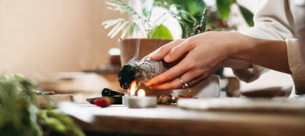 naine hoiab tossavat valge salvei kimpu enne ritaalset puhastust. Laual on põlevad küünlad ja rohelised taimed. Salvei toss puhastamas kristalle ja stressi, viies eemale negatiivse energia